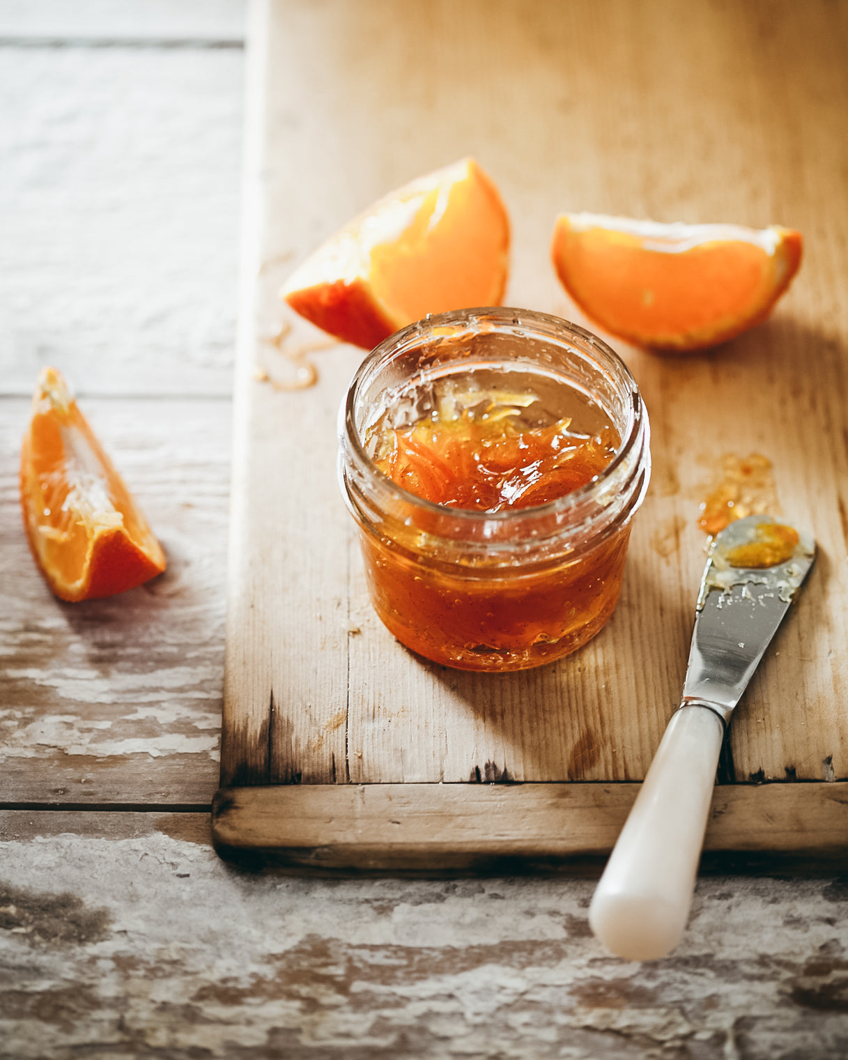 Brilliant orange kumquat marmalade in a glass jar on a wooden board.