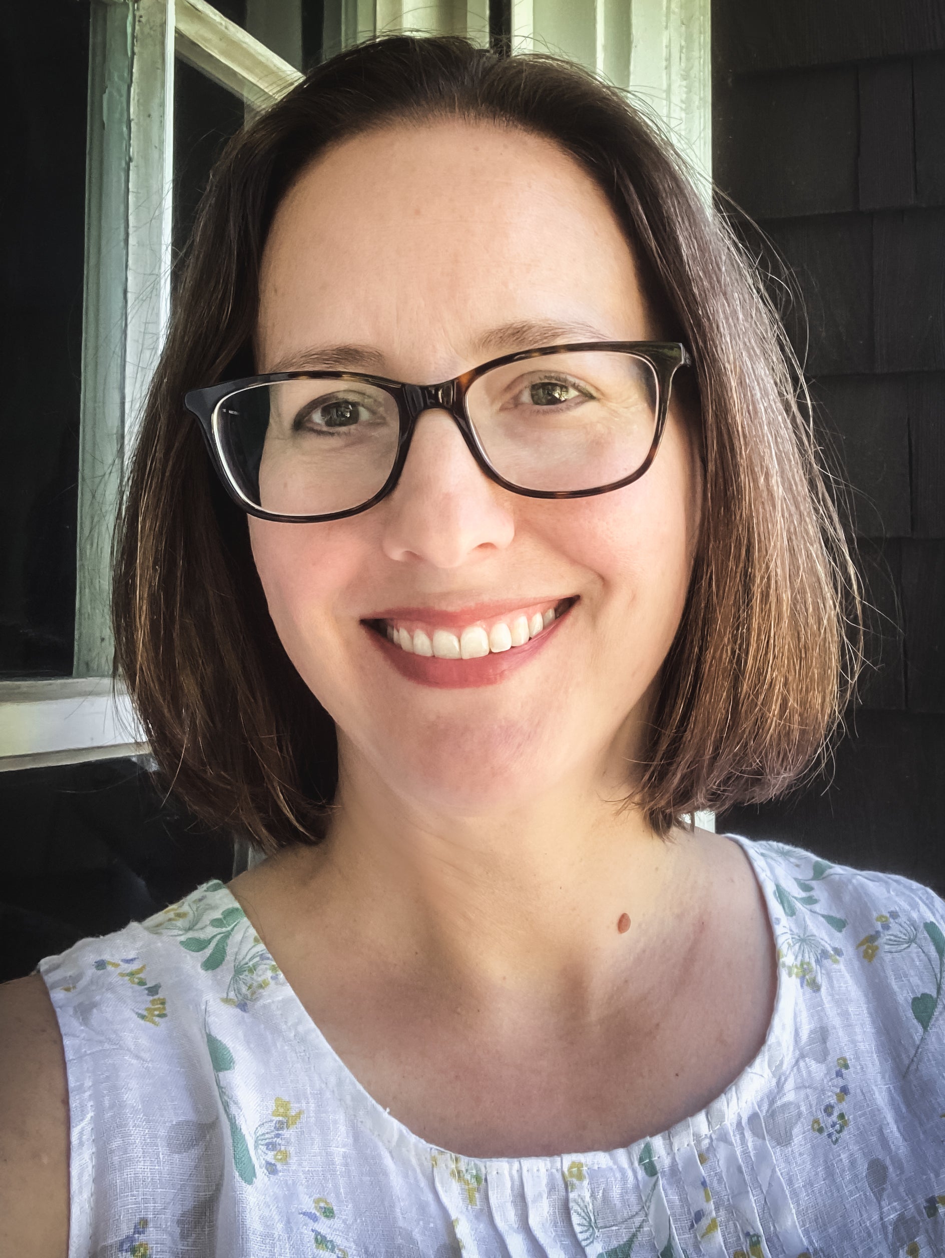 Female author wearing glasses and a floral blouse, smiling outdoors.